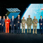Officials and Polish Army officers on stage at the POLSARIS handover ceremony, with a SAR satellite render and the Polish flag on the screen behind them