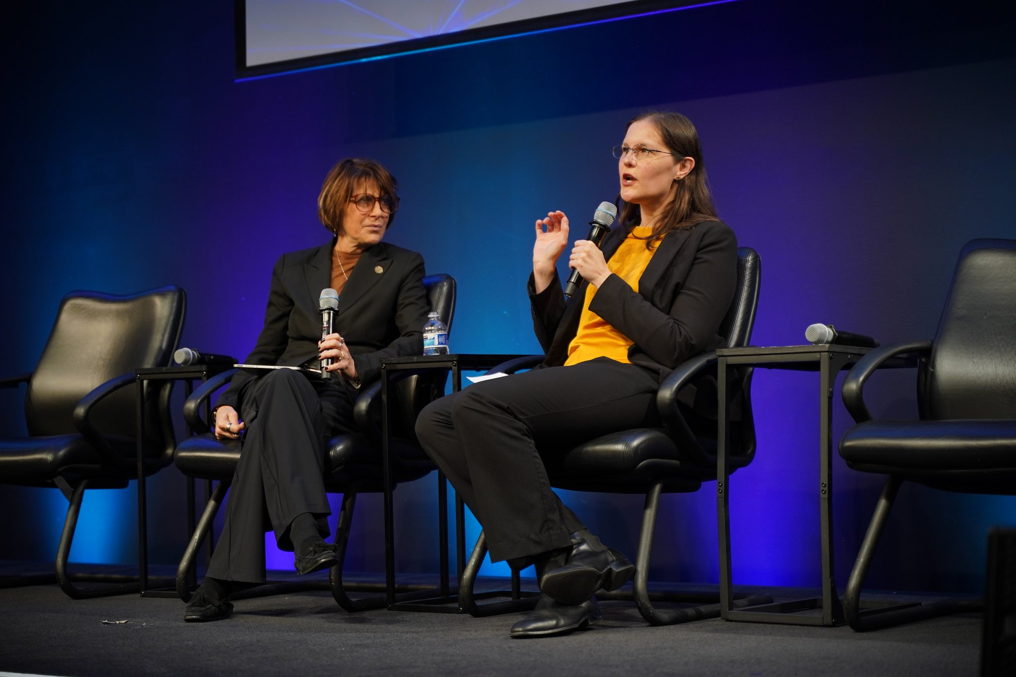 Katherine Coens of Space Systems Command speaks into a microphone beside retired Maj. Gen. Kimberly Crider during their interview at the MilSat Symposium at Silicon Valley Space Week 2026.